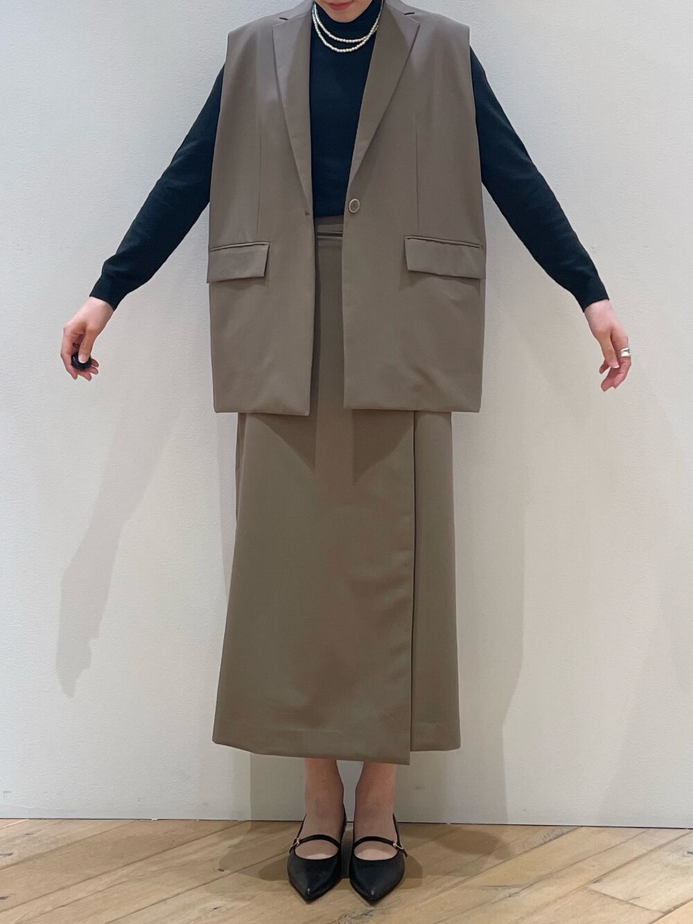 ブラウン系のベスト、ブラック系のパンプス、ブラウン系のスカートを着用したレディースの冬コーディネートの6枚目の写真