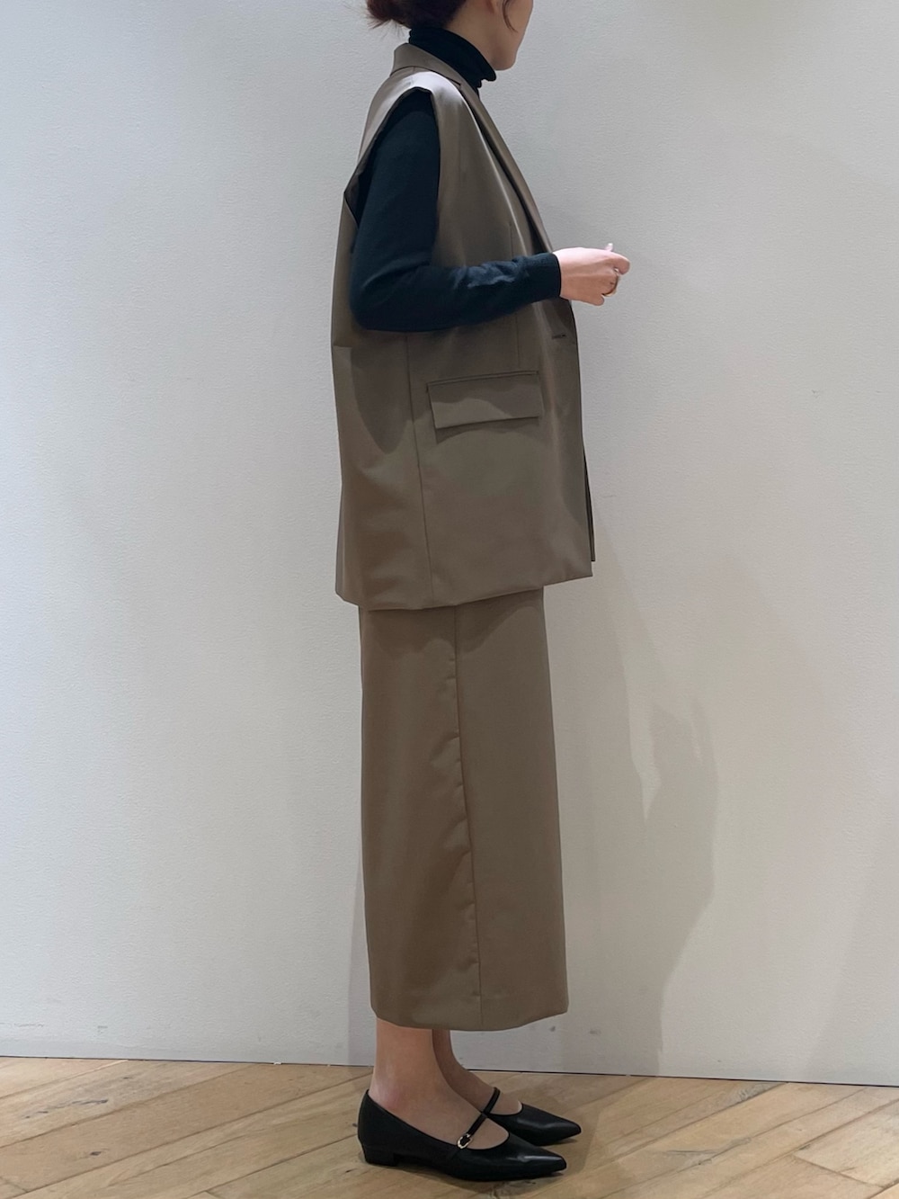 ブラウン系のベスト、ブラック系のパンプス、ブラウン系のスカートを着用したレディースの冬コーディネートの2枚目の写真