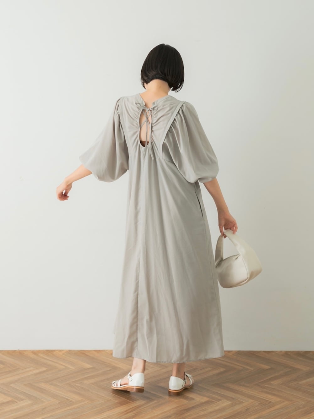 グレー系のワンピース、ホワイト系のハンドバッグ、ホワイト系のサンダルを着用したレディースの夏コーディネートの3枚目の写真