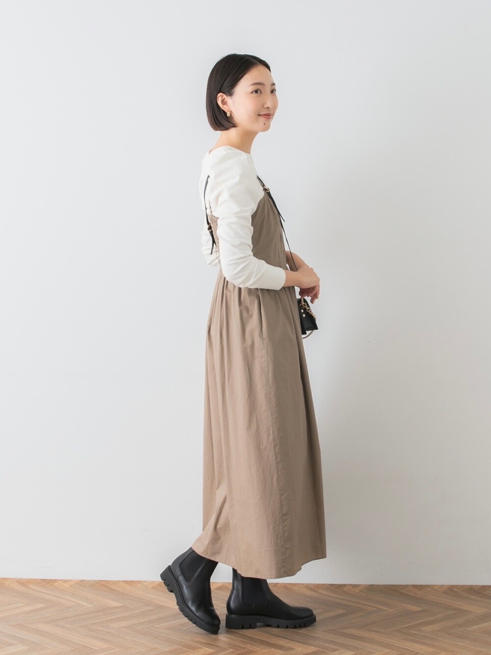 ベージュ系のワンピース、ホワイト系のTシャツ/カットソー、ブラック系のブーツを着用したレディースの秋コーディネートの2枚目の写真