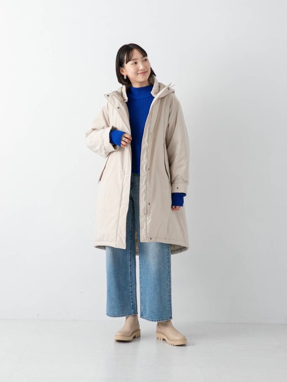 ブルー系のデニムパンツ、ベージュ系のダウンジャケット/コート、ブルー系のニット/セーターを着用したレディースの冬コーディネートの2枚目の写真