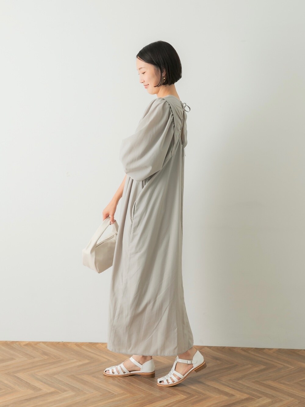グレー系のワンピース、ホワイト系のハンドバッグ、ホワイト系のサンダルを着用したレディースの夏コーディネートの2枚目の写真