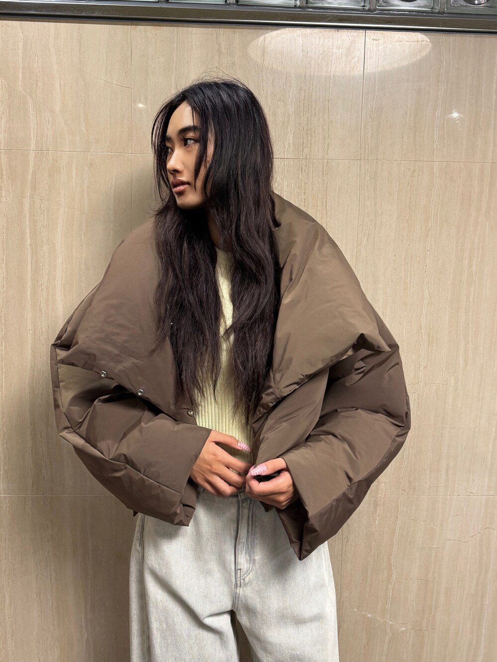 イエロー系のニット/セーター、ブラウン系のダウンジャケット/コート、ホワイト系のデニムパンツを着用したレディースの冬コーディネートの3枚目の写真