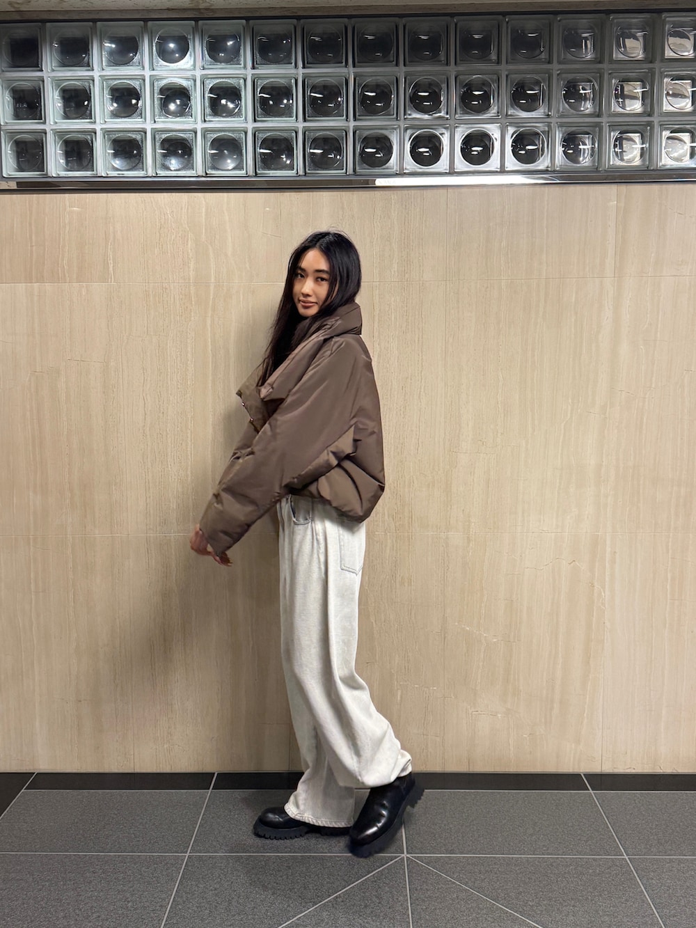 イエロー系のニット/セーター、ブラウン系のダウンジャケット/コート、ホワイト系のデニムパンツを着用したレディースの冬コーディネートの2枚目の写真