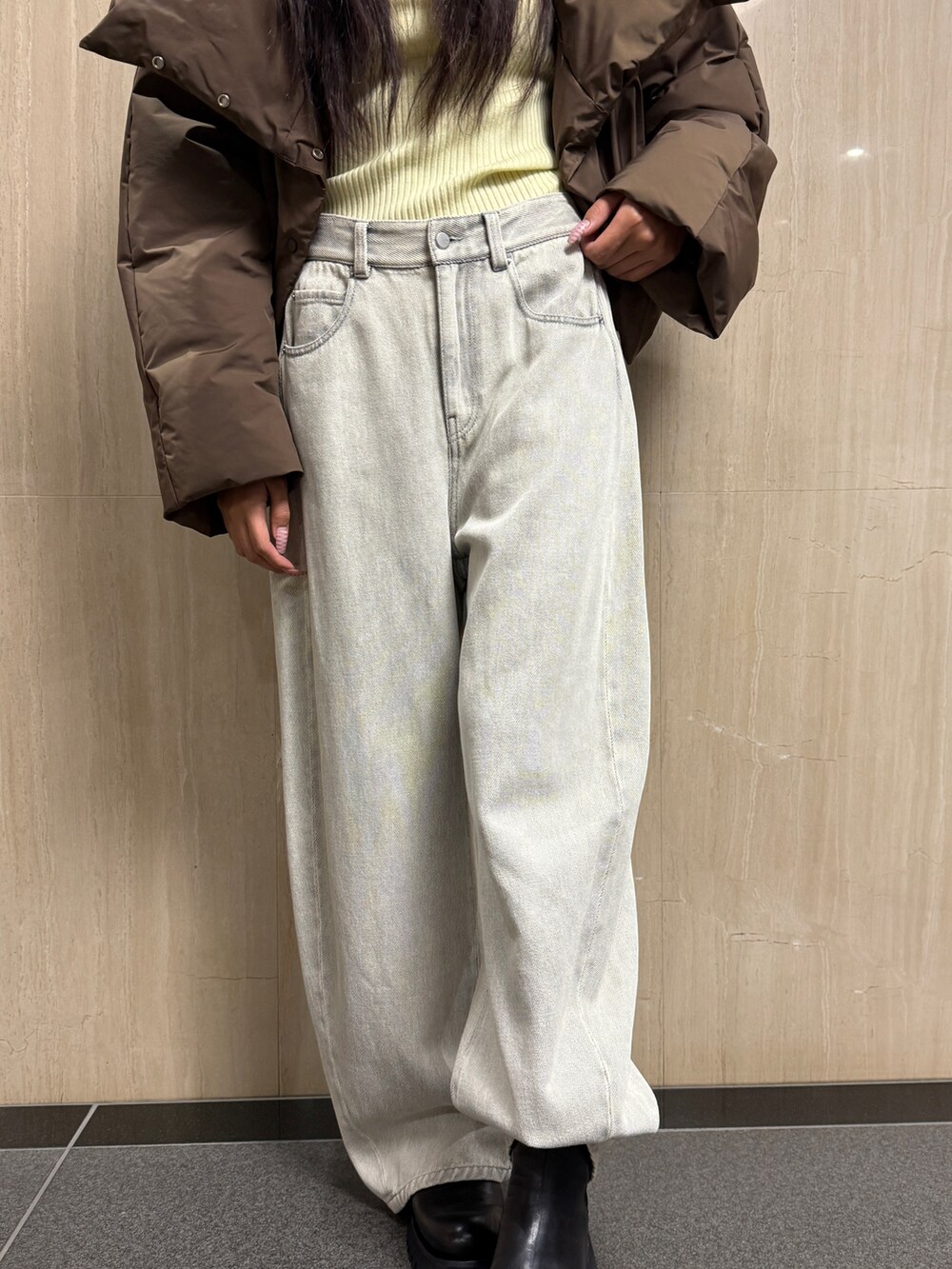 イエロー系のニット/セーター、ブラウン系のダウンジャケット/コート、ホワイト系のデニムパンツを着用したレディースの冬コーディネートの4枚目の写真