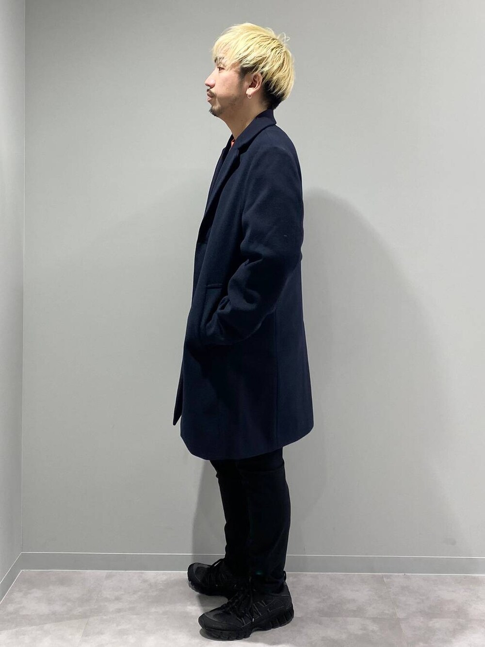 ブラック系のその他パンツ、ブルー系のチェスターコート、オレンジ系のスウェットを着用したメンズの冬コーディネートの2枚目の写真