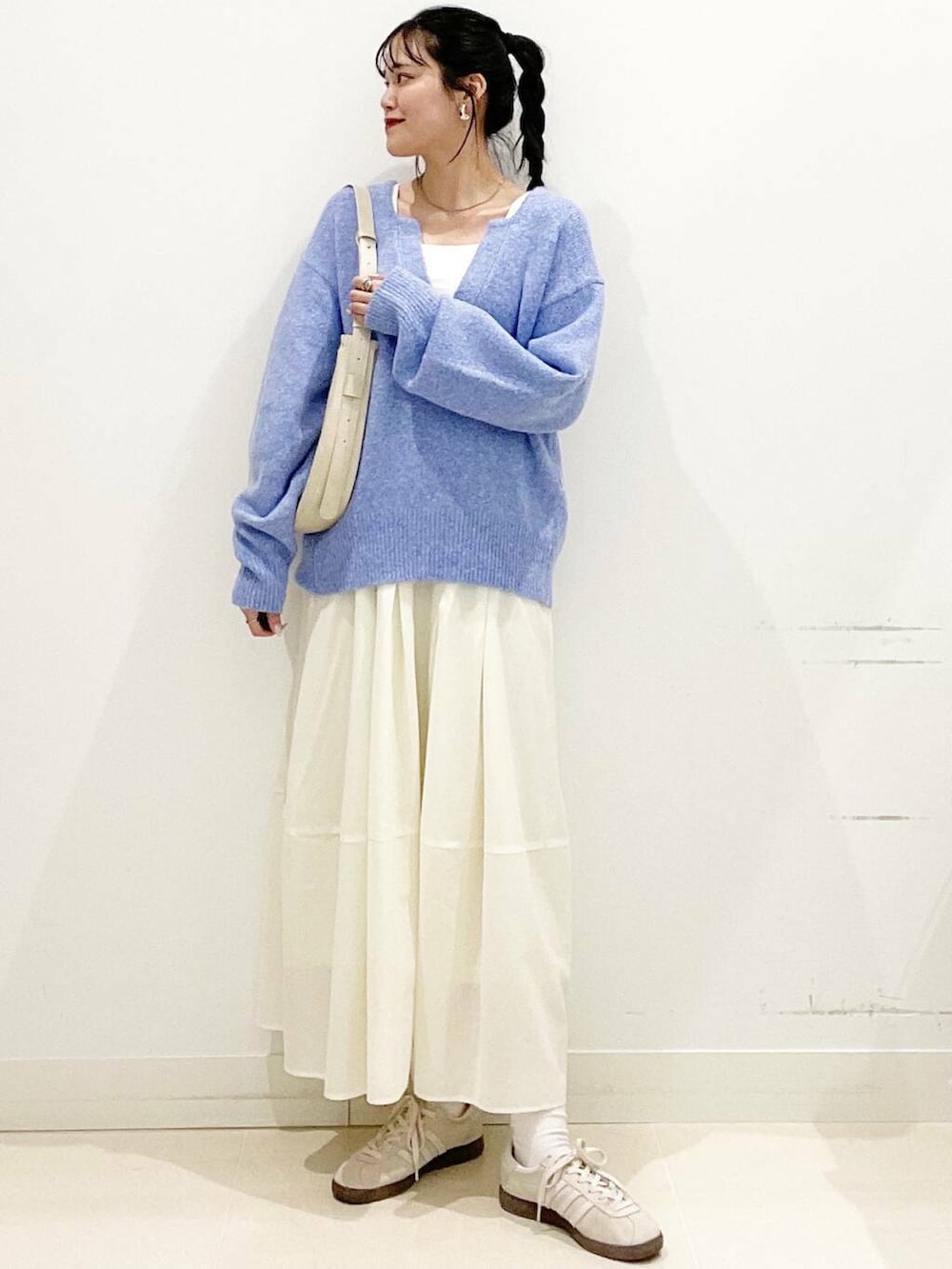 ホワイト系のスニーカー、ブルー系のニット/セーター、ベージュ系のショルダーバッグを着用したレディースの春コーディネートの3枚目の写真
