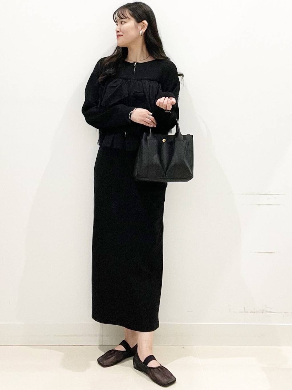 ブラック系のニット/セーター、ブラック系のスカート、ブラック系のトートバッグを着用したレディースの春コーディネートの2枚目の写真