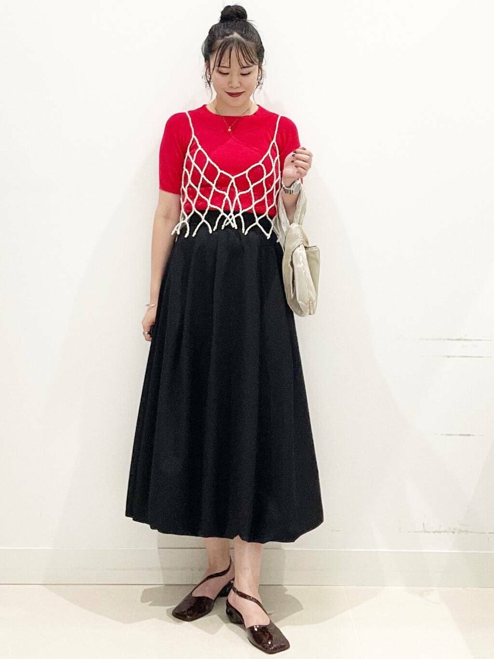 ブラック系のスカート、ゴールド系のハンドバッグ、レッド系のニット/セーターを着用したレディースの夏コーディネートの5枚目の写真