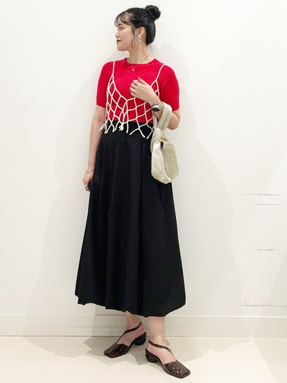 ブラック系のスカート、ゴールド系のハンドバッグ、レッド系のニット/セーターを着用したレディースの夏コーディネートの3枚目の写真