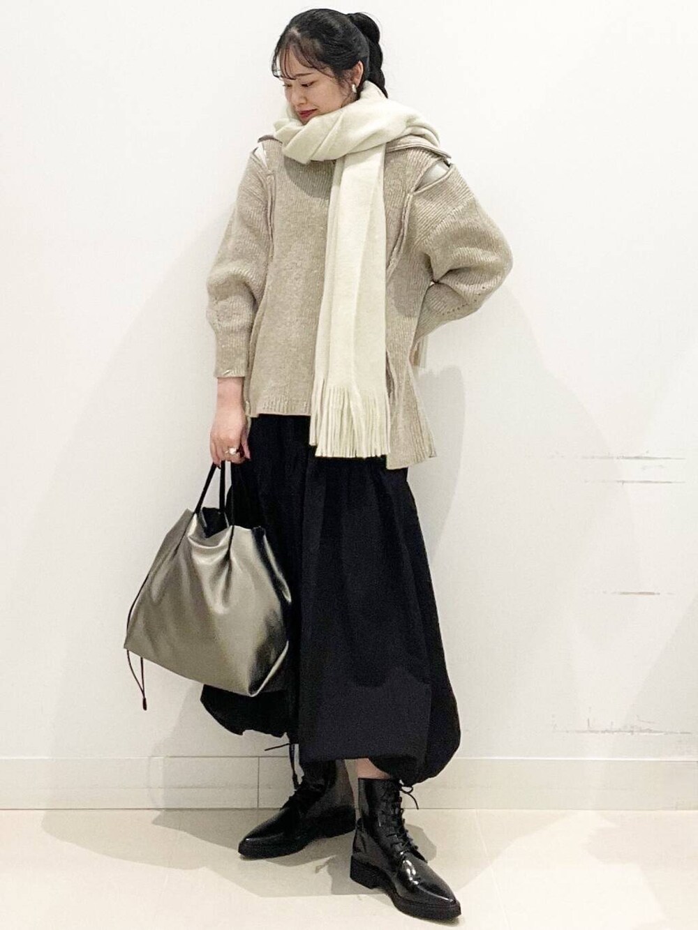 シルバー系のトートバッグ、ベージュ系のニット/セーター、ブラック系のスカートを着用したレディースの冬コーディネートの3枚目の写真