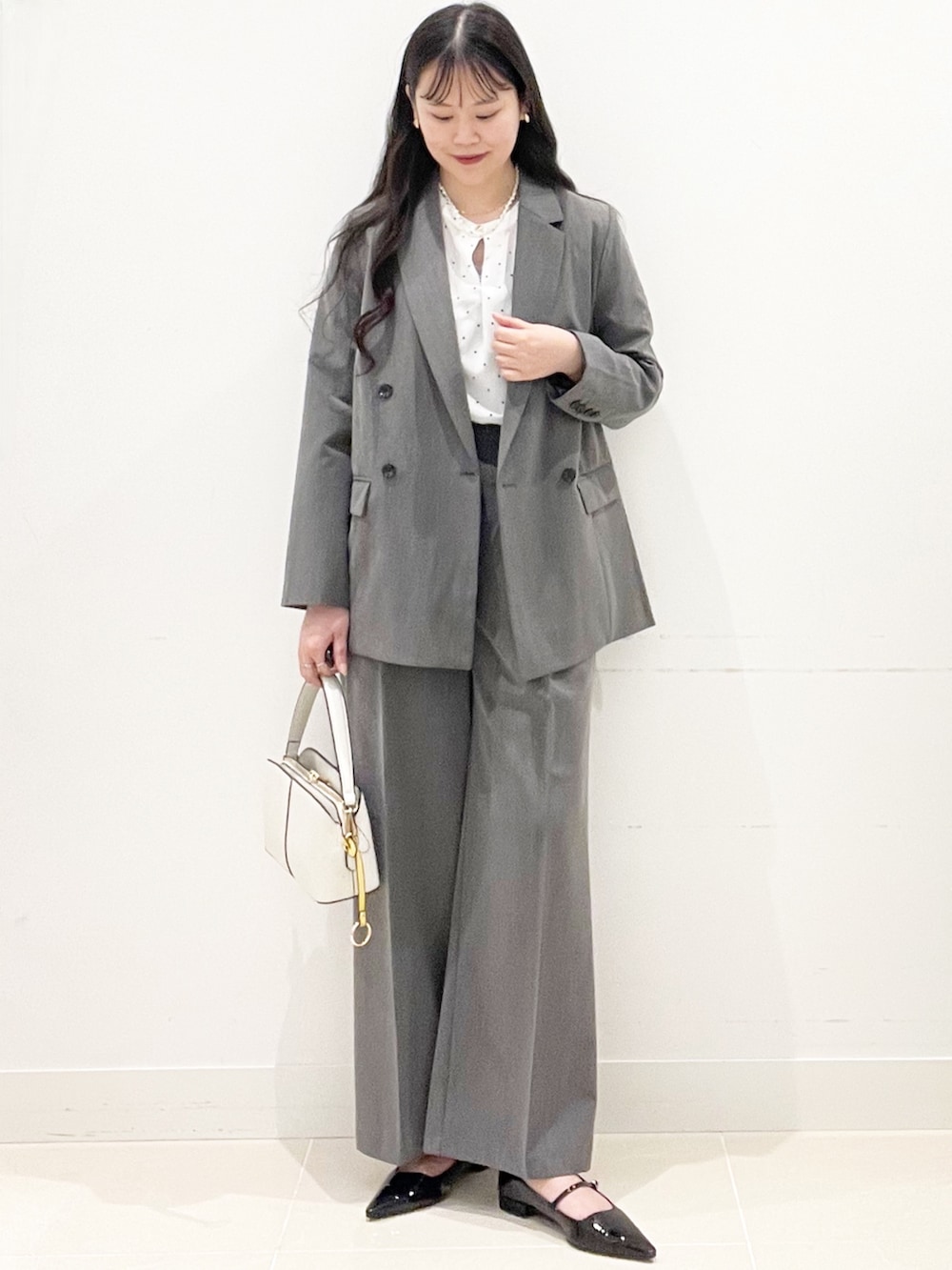 ブラック系のパンプス、グレー系のスラックス、ホワイト系のハンドバッグを着用したレディースの冬コーディネートの3枚目の写真