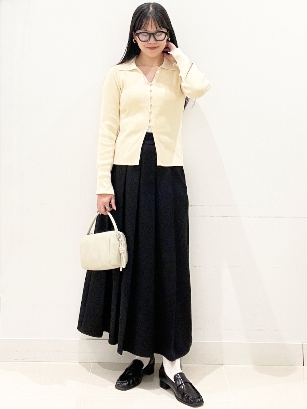 ブラック系のローファー、ブラック系のスカート、ベージュ系のハンドバッグを着用したレディースの春コーディネートの2枚目の写真
