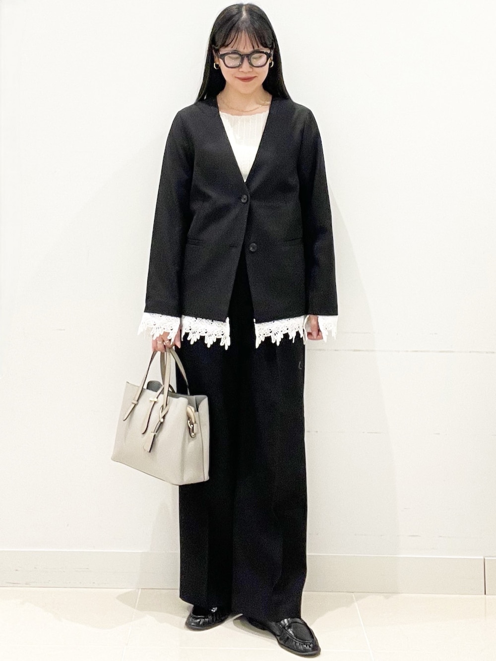 ブラック系のスラックス、グレー系のトートバッグ、ブラック系のノーカラージャケットを着用したレディースの春コーディネートの3枚目の写真