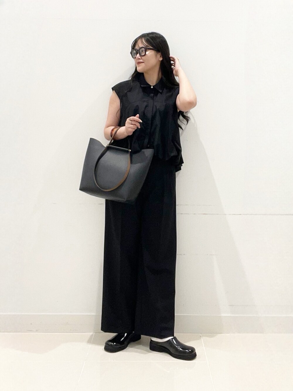 ブラック系のスラックス、ブラック系のサンダル、ブラック系のビジネスバッグを着用したレディースの夏コーディネートの2枚目の写真