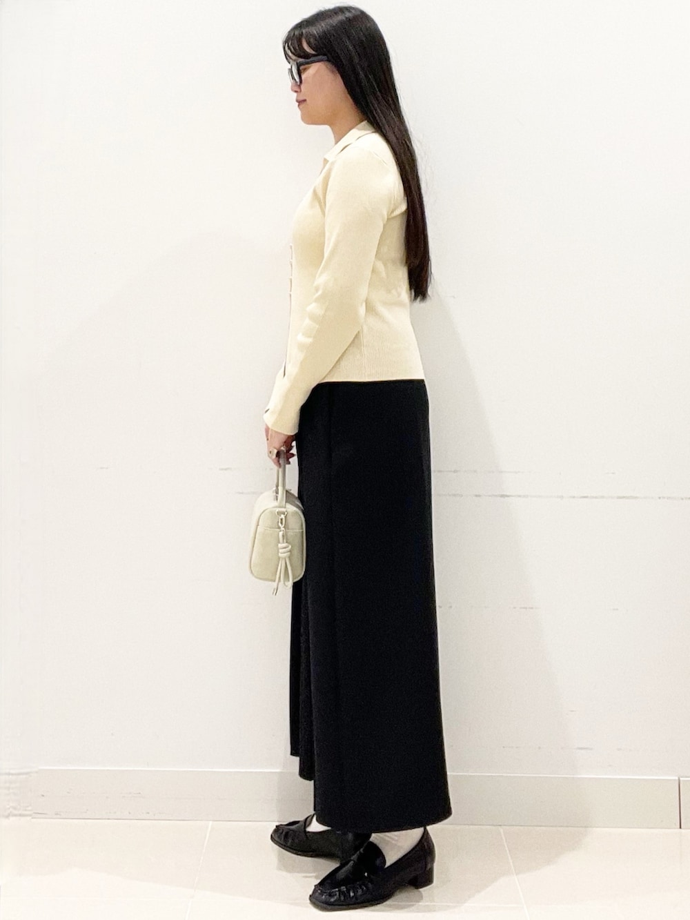 ブラック系のローファー、ブラック系のスカート、ベージュ系のハンドバッグを着用したレディースの春コーディネートの3枚目の写真