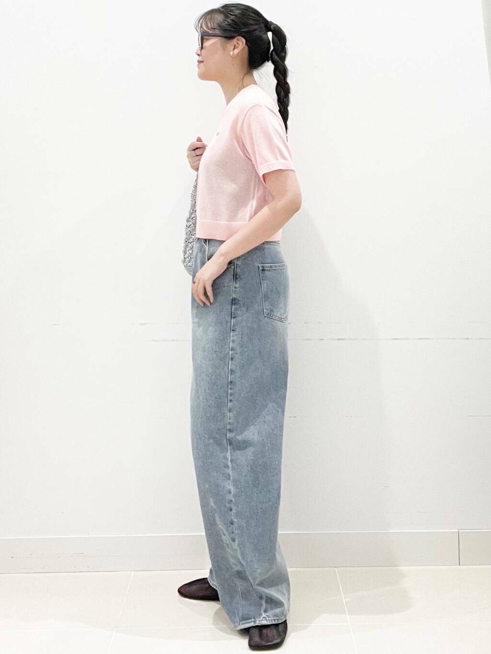 シルバー系のハンドバッグ、ブラック系のパンプス、ブルー系のデニムパンツを着用したレディースの夏コーディネートの4枚目の写真