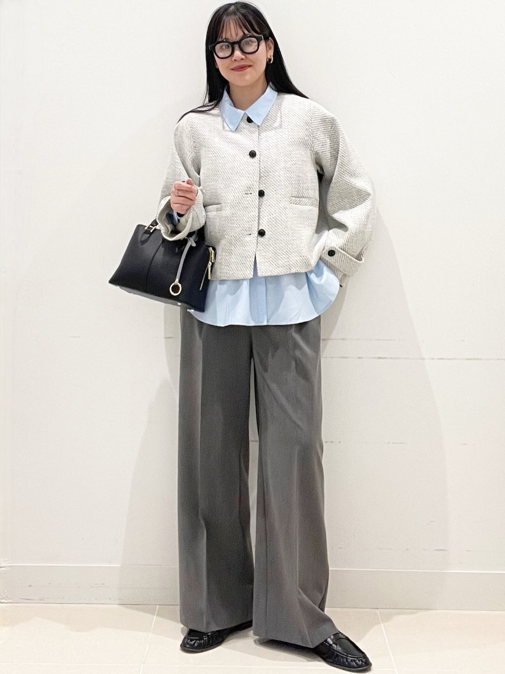 グレー系のスラックス、ブラック系のハンドバッグ、ブルー系のシャツ/ブラウスを着用したレディースの春コーディネートの2枚目の写真
