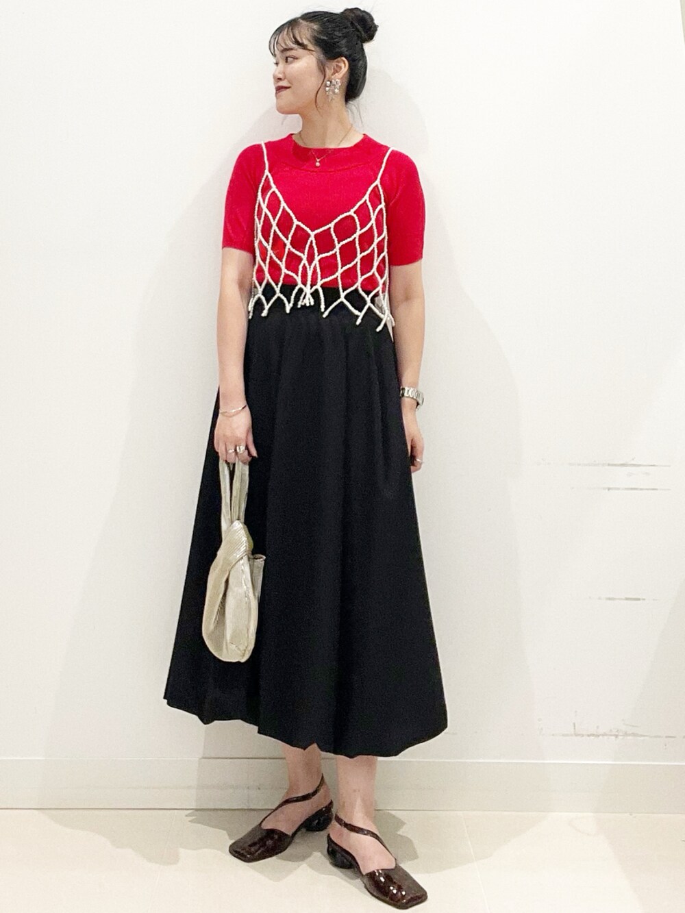 ブラック系のスカート、ゴールド系のハンドバッグ、レッド系のニット/セーターを着用したレディースの夏コーディネートの2枚目の写真