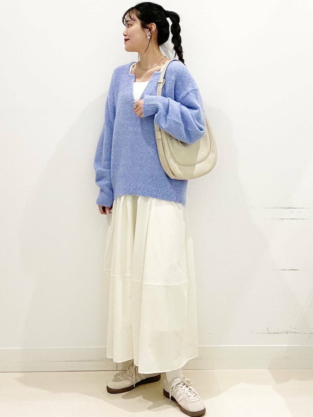 ホワイト系のスニーカー、ブルー系のニット/セーター、ベージュ系のショルダーバッグを着用したレディースの春コーディネートの2枚目の写真