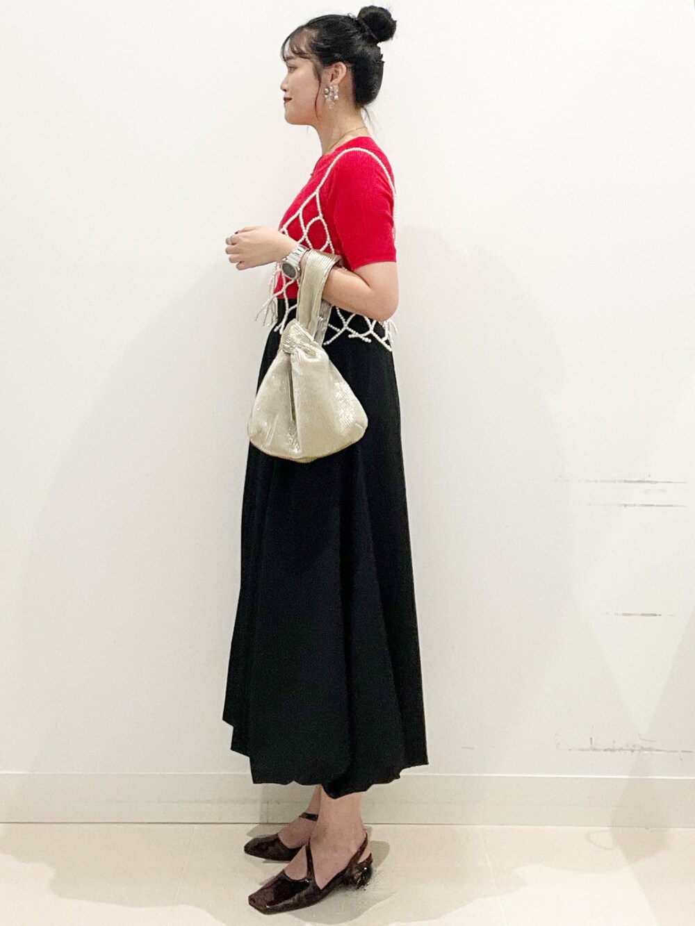 ブラック系のスカート、ゴールド系のハンドバッグ、レッド系のニット/セーターを着用したレディースの夏コーディネートの6枚目の写真