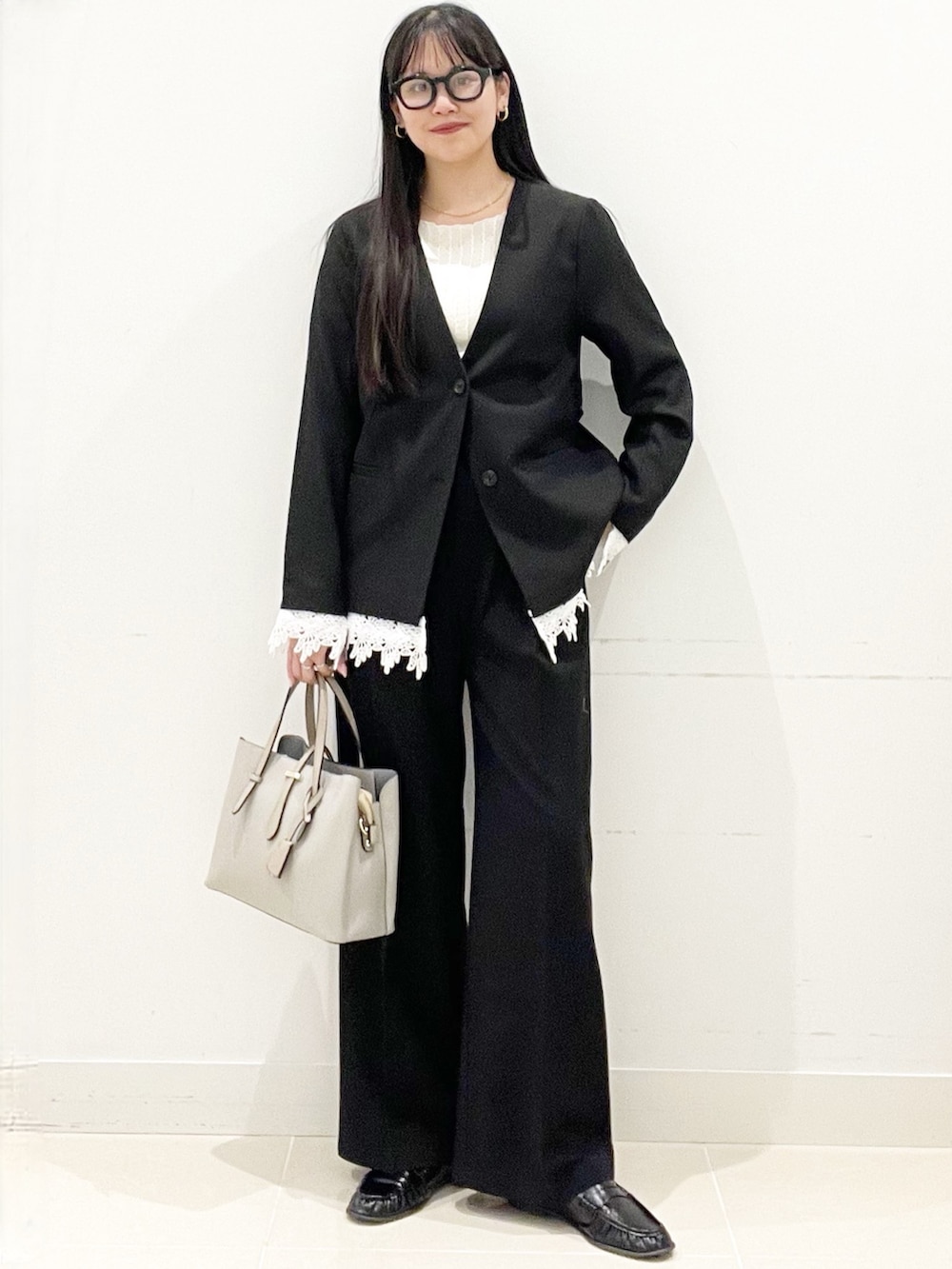 ブラック系のスラックス、グレー系のトートバッグ、ブラック系のノーカラージャケットを着用したレディースの春コーディネートの2枚目の写真