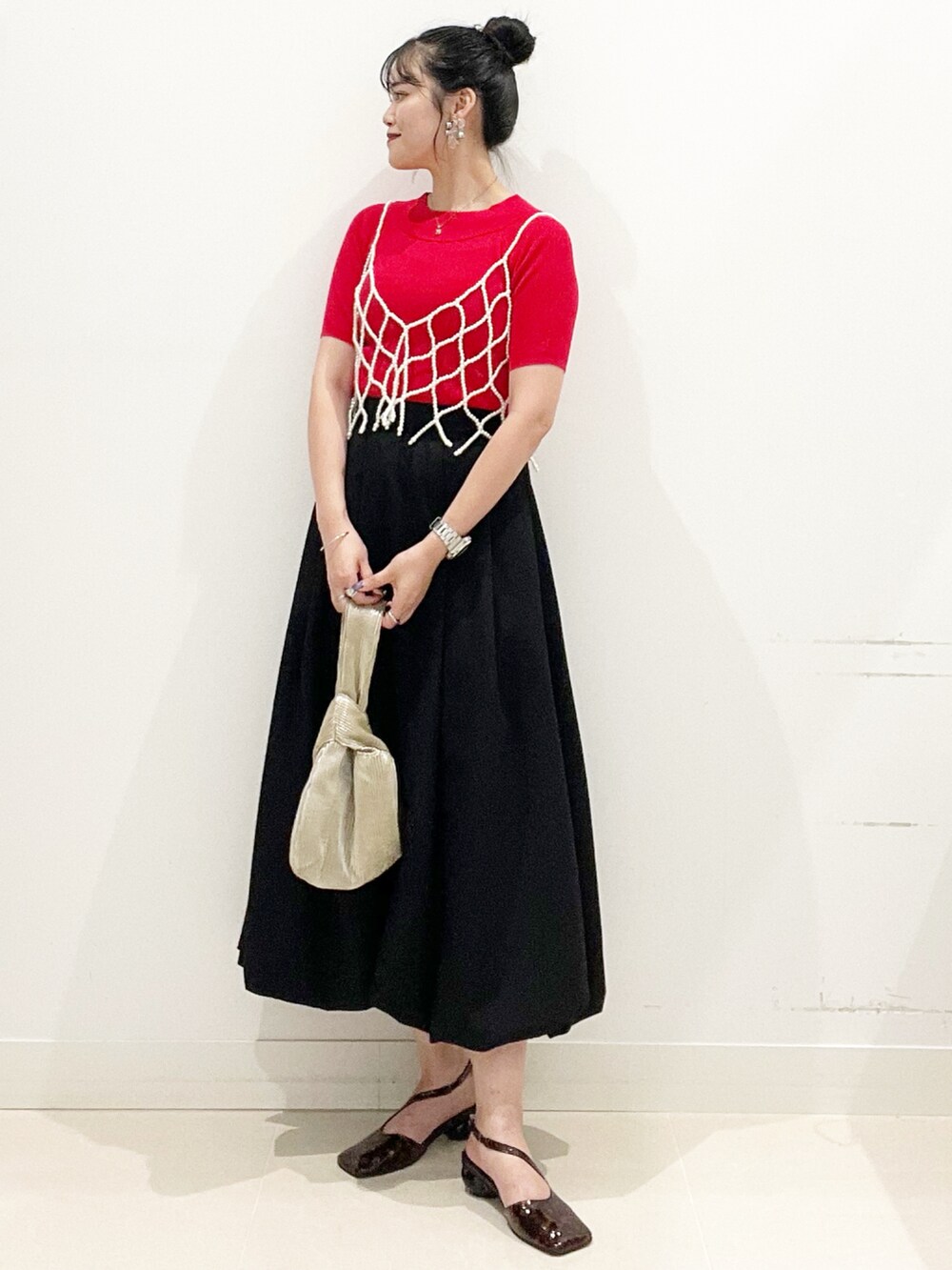 ブラック系のスカート、ゴールド系のハンドバッグ、レッド系のニット/セーターを着用したレディースの夏コーディネートの4枚目の写真