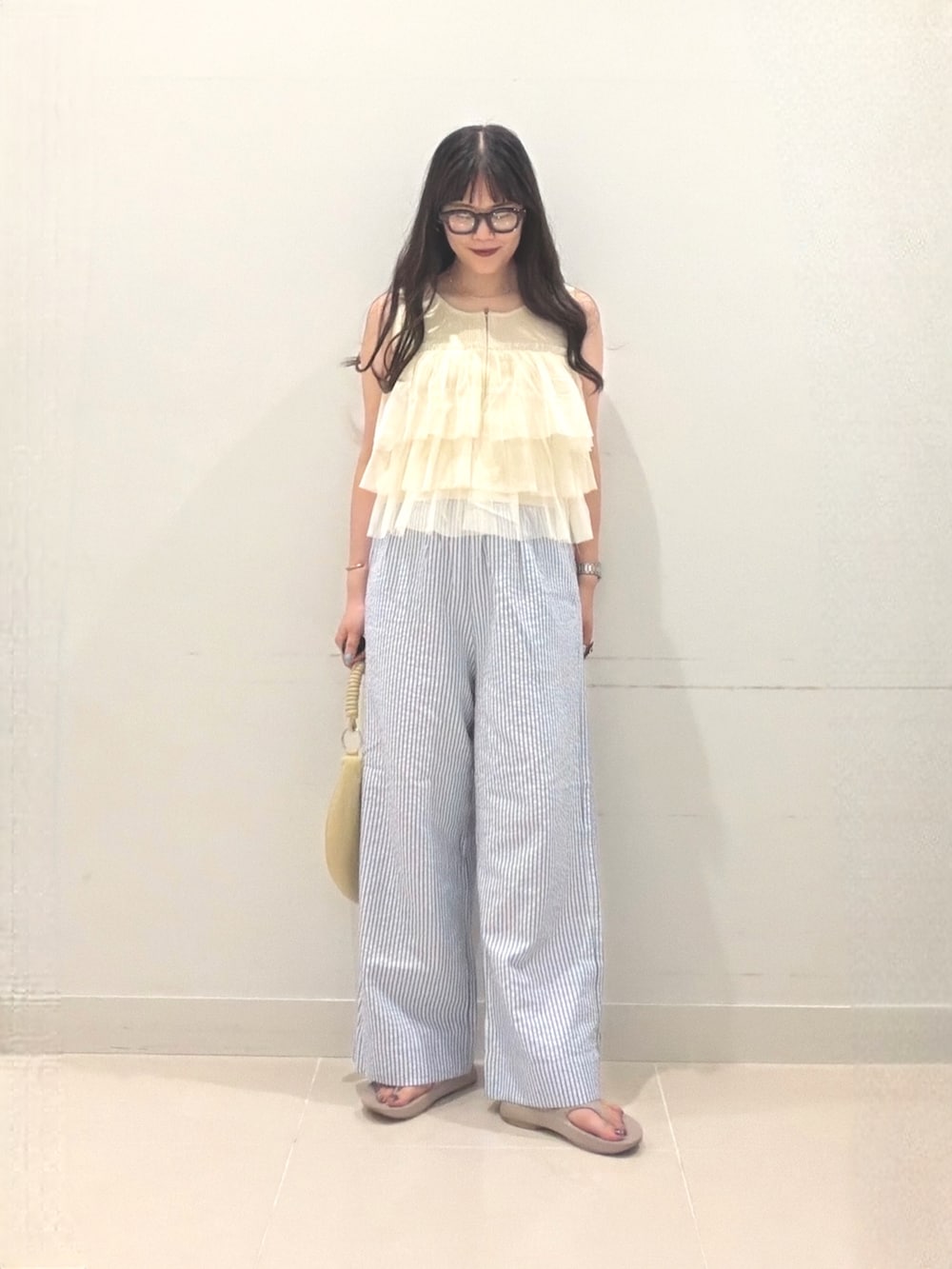 イエロー系のニット/セーター、ベージュ系のハンドバッグ、ベージュ系のサンダルを着用したレディースの夏コーディネートの3枚目の写真