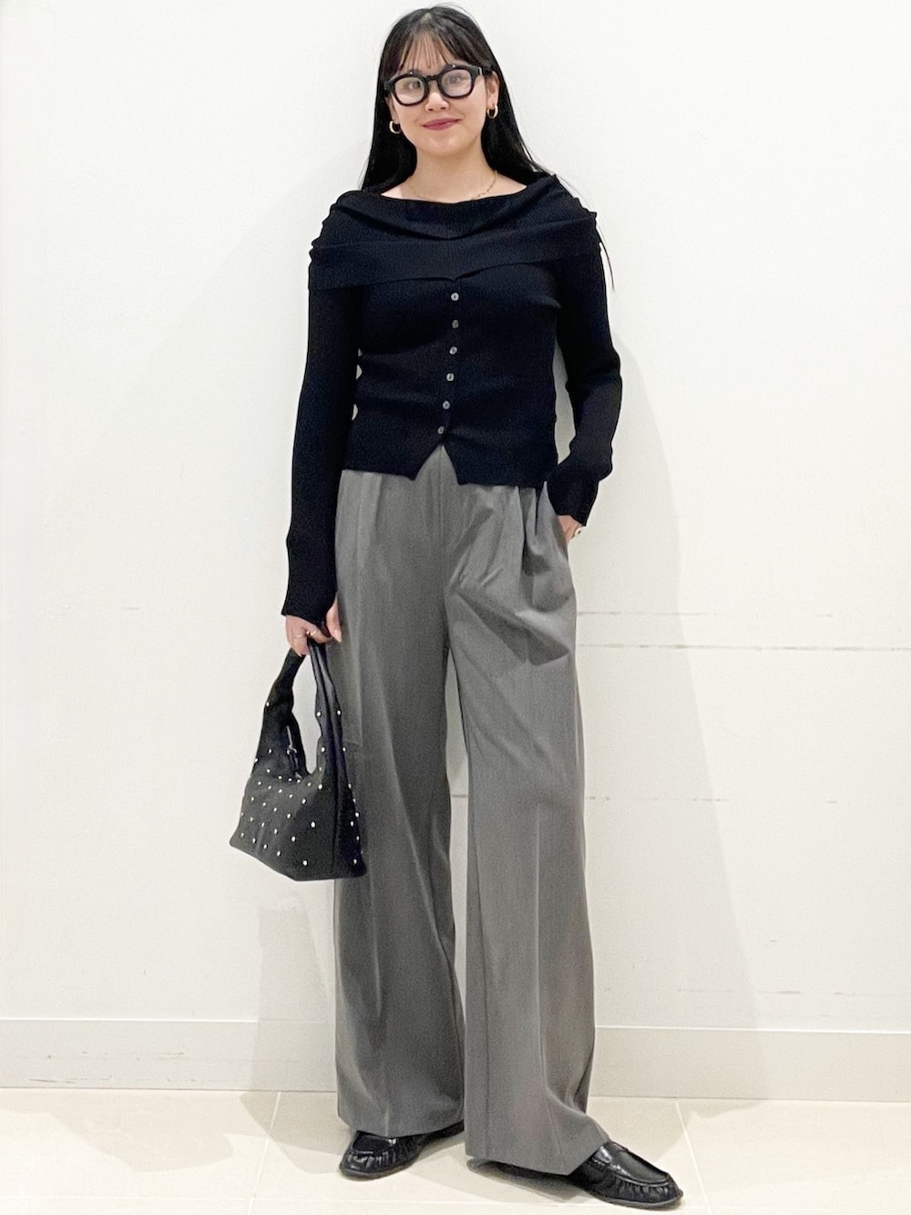 グレー系のスラックス、ブラック系のハンドバッグ、ブラック系のニット/セーターを着用したレディースの春コーディネートの2枚目の写真