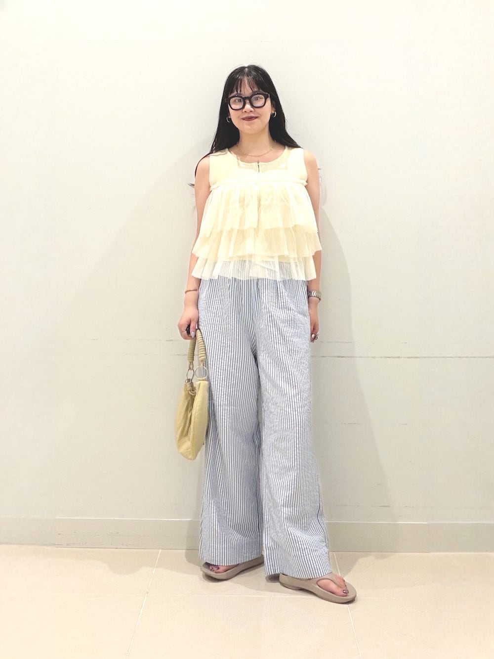 イエロー系のニット/セーター、ベージュ系のハンドバッグ、ベージュ系のサンダルを着用したレディースの夏コーディネートの2枚目の写真