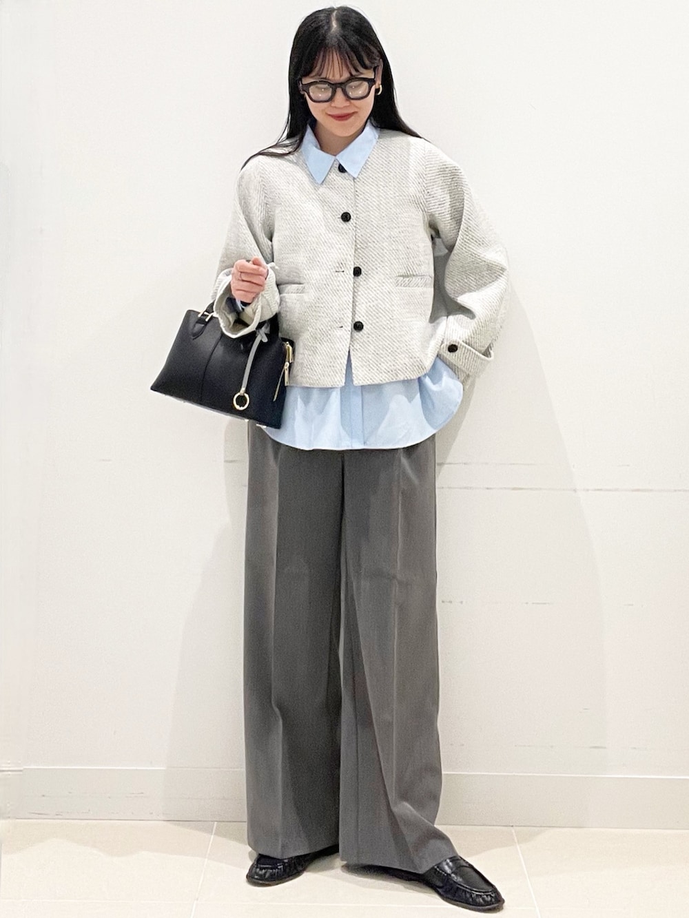 グレー系のスラックス、ブラック系のハンドバッグ、ブルー系のシャツ/ブラウスを着用したレディースの春コーディネートの3枚目の写真