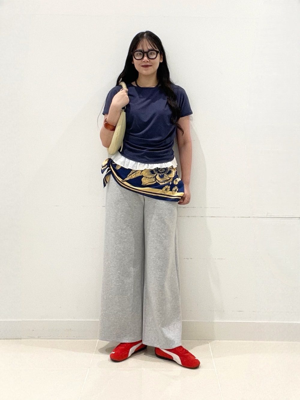 グレー系のスラックス、レッド系のスニーカー、ベージュ系のハンドバッグを着用したレディースの夏コーディネートの2枚目の写真