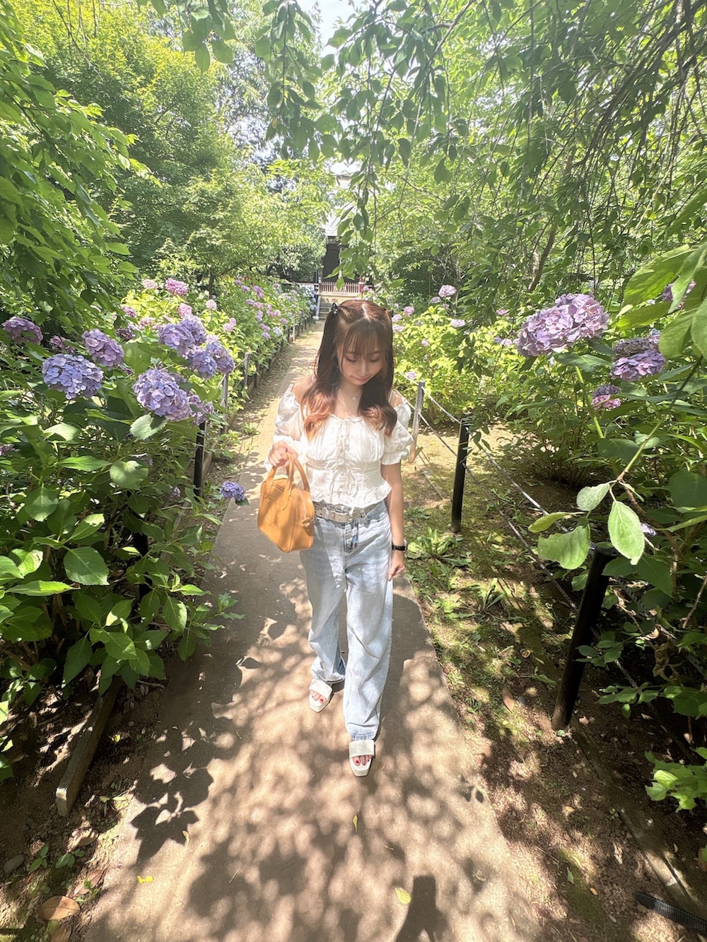 イエロー系のハンドバッグ、ホワイト系のシャツ/ブラウス、ブルー系のデニムパンツを着用したレディースの夏コーディネートの7枚目の写真