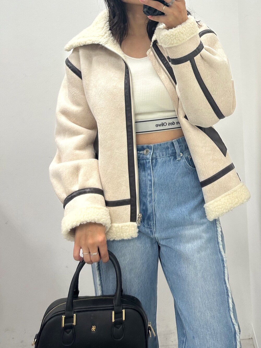 ホワイト系のライダースジャケット、ブラック系のショルダーバッグ、ブルー系のデニムパンツを着用したレディースの秋コーディネートの2枚目の写真