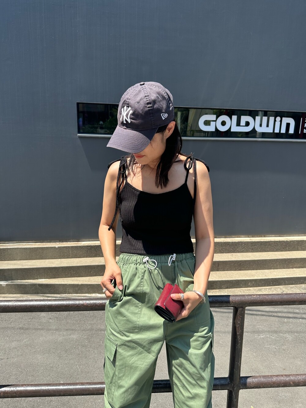 グリーン系のカーゴパンツ、ブラック系のキャミソール、ブルー系のキャップを着用したレディースの夏コーディネートの2枚目の写真