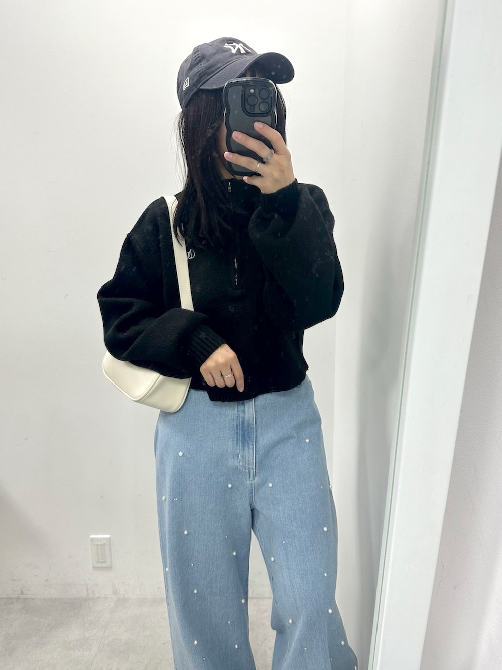 ブルー系のデニムパンツ、ブラック系のニット/セーター、ホワイト系のショルダーバッグを着用したレディースの冬コーディネートの2枚目の写真