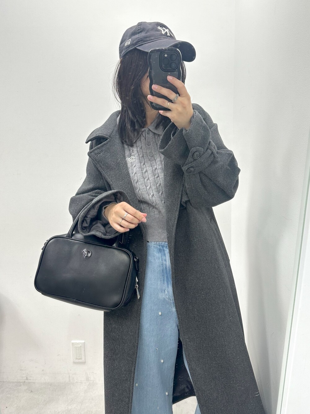 グレー系のステンカラーコート、グレー系のニット/セーター、ブラック系のショルダーバッグを着用したレディースの冬コーディネートの2枚目の写真