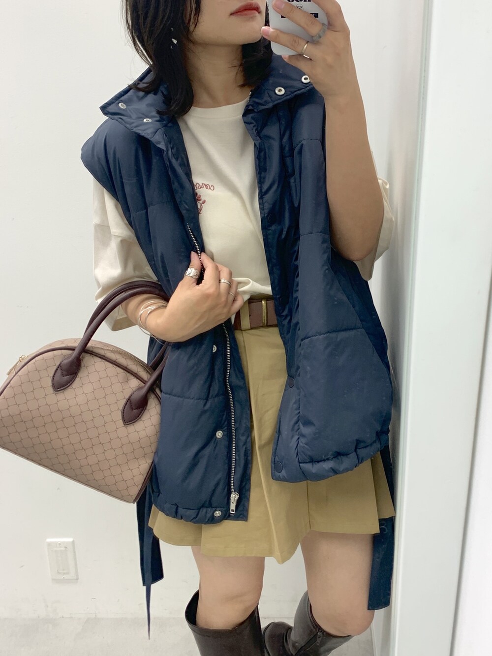 ベージュ系のスカート、ブルー系のダウンベスト、ホワイト系のTシャツ/カットソーを着用したレディースの夏コーディネートの2枚目の写真