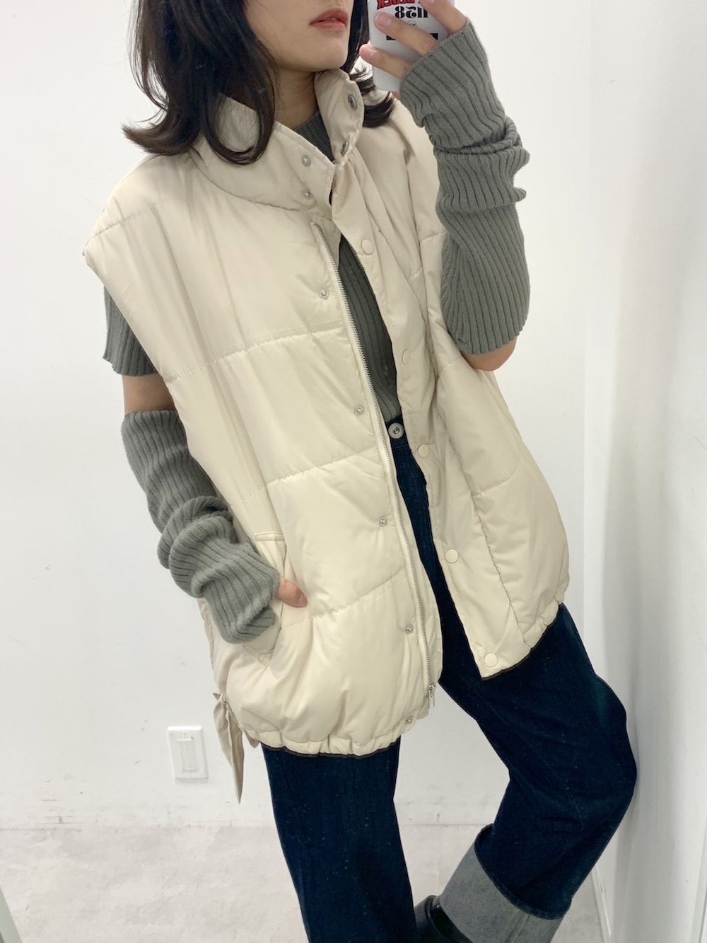 ブルー系のデニムパンツ、グリーン系のニット/セーター、ホワイト系のダウンベストを着用したレディースの夏コーディネートの2枚目の写真