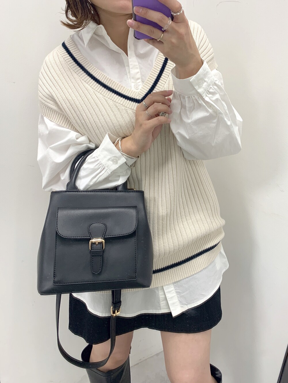 ブラック系のブーツ、ブラック系のショルダーバッグ、ホワイト系のベストを着用したレディースの冬コーディネートの2枚目の写真