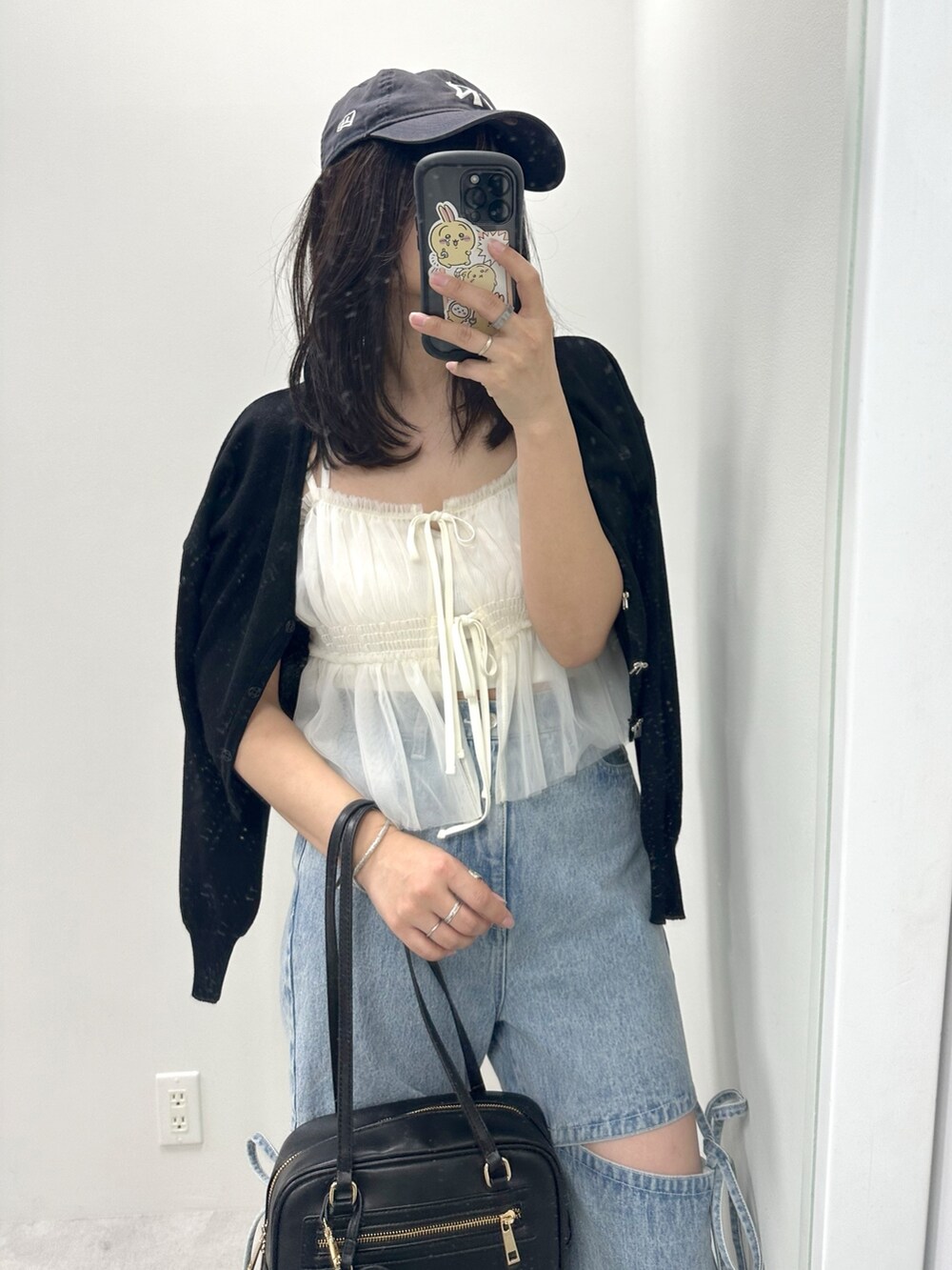 ブルー系のデニムパンツ、ホワイト系のキャミソール、ブラック系のカーディガン/ボレロを着用したレディースの春コーディネートの2枚目の写真