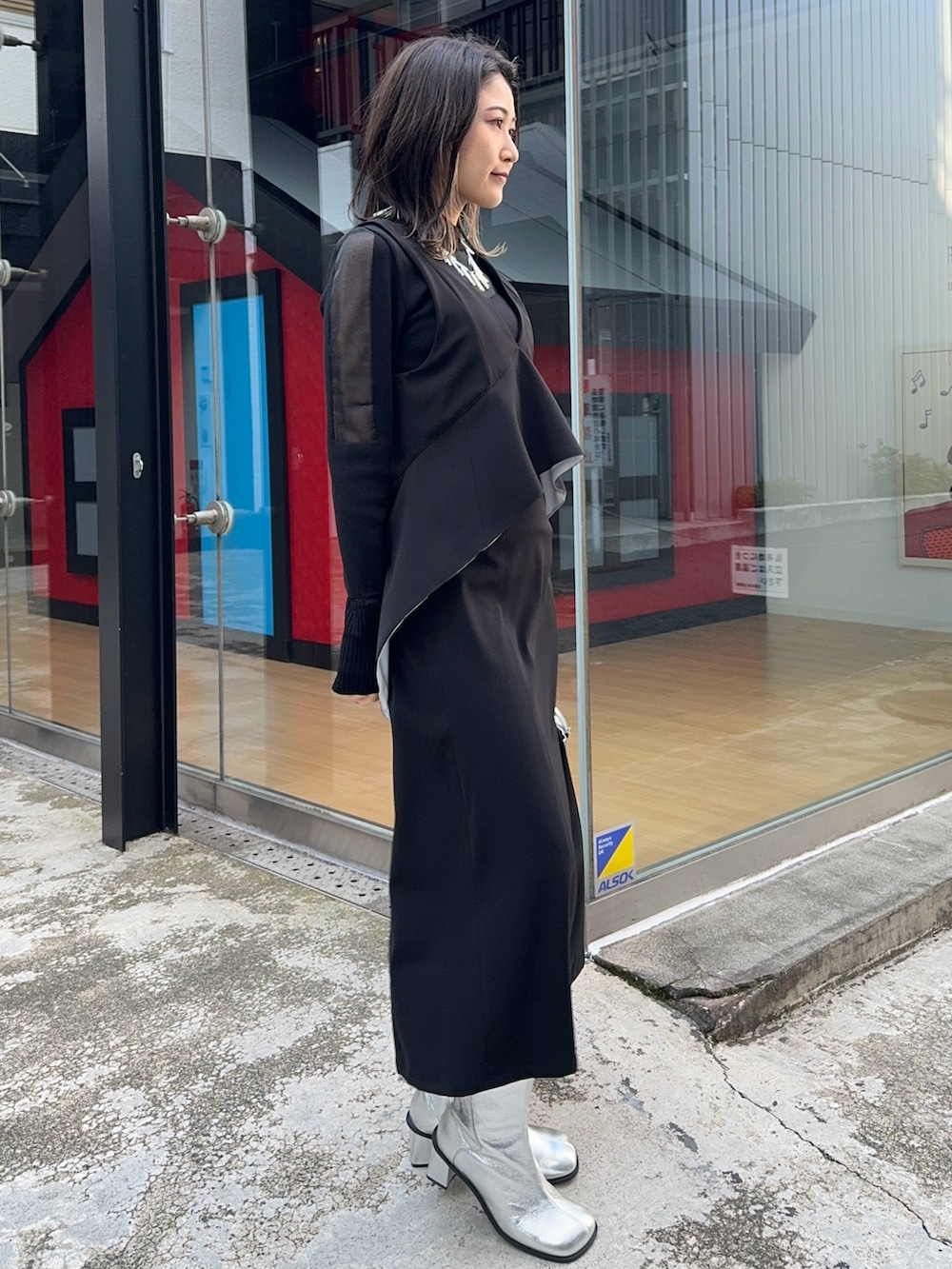 ブラック系のジャンパースカート、ブラック系のニット/セーター、シルバー系のショルダーバッグを着用したレディースの冬コーディネートの2枚目の写真