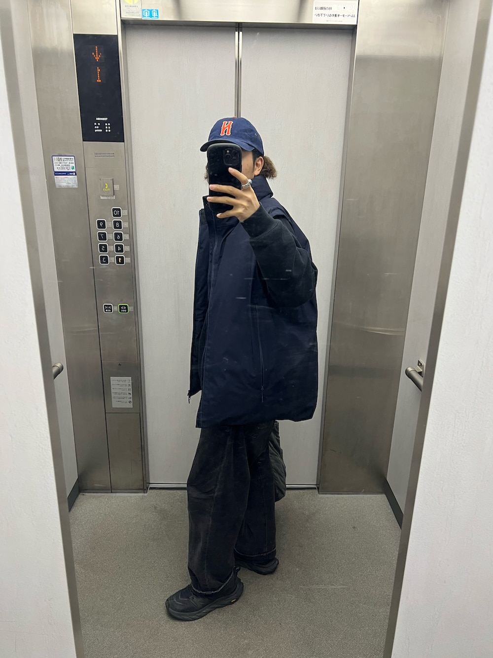 ブルー系のダウンベスト、グレー系のトートバッグ、ブラック系のスニーカーを着用したメンズの春コーディネートの2枚目の写真