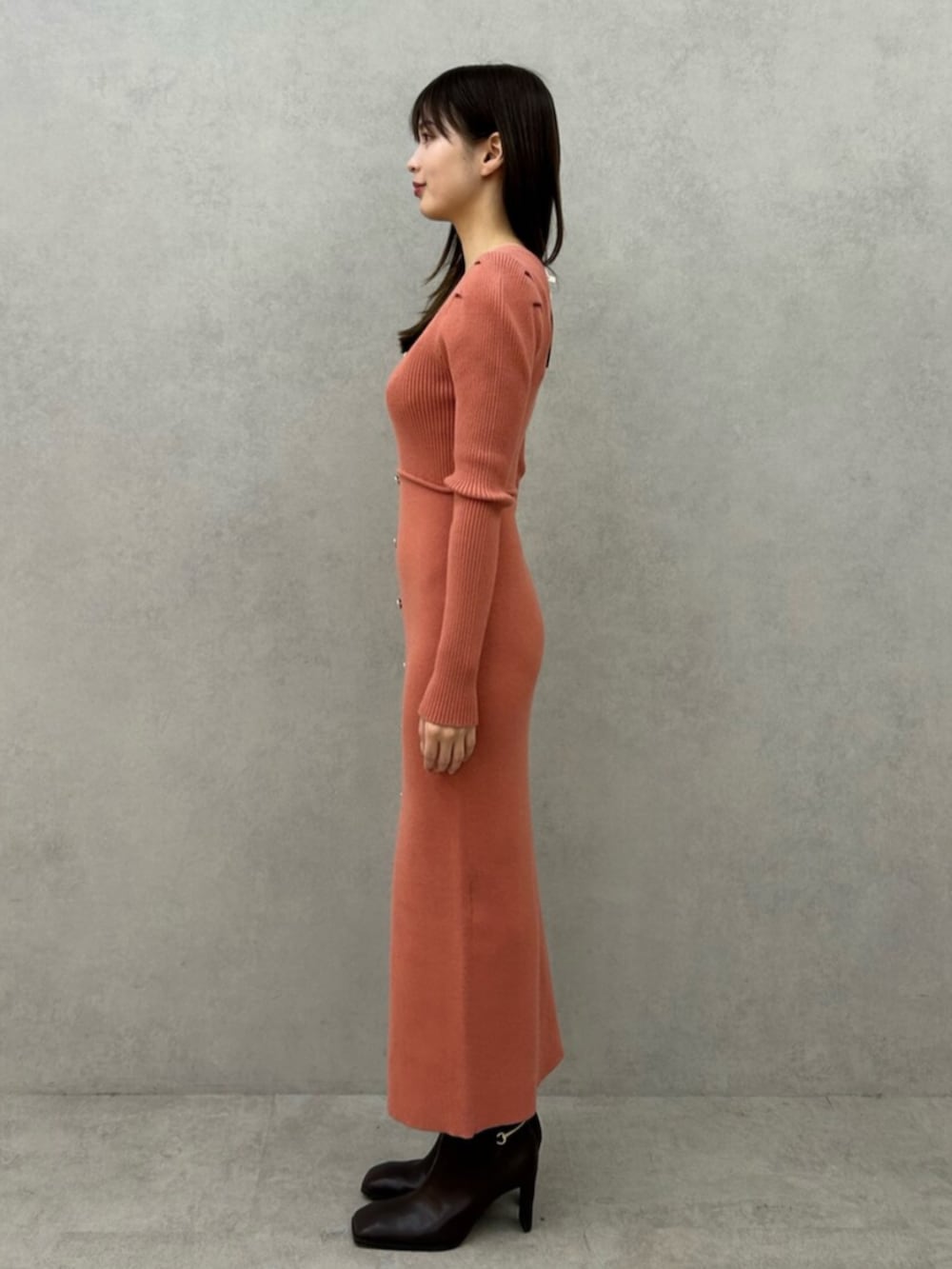 オレンジ系のワンピース、ブラック系のブーツを着用したレディースの冬コーディネートの2枚目の写真