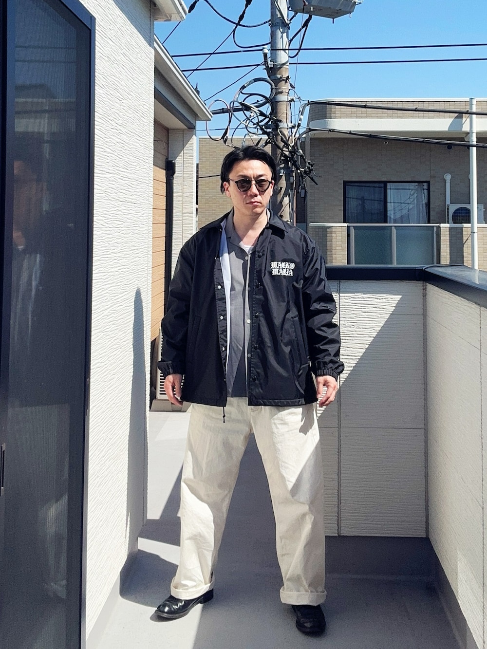 グレー系のシャツ/ブラウス、ブラック系のジャケット/アウター、ホワイト系のチノパンツを着用したメンズの春コーディネートの2枚目の写真