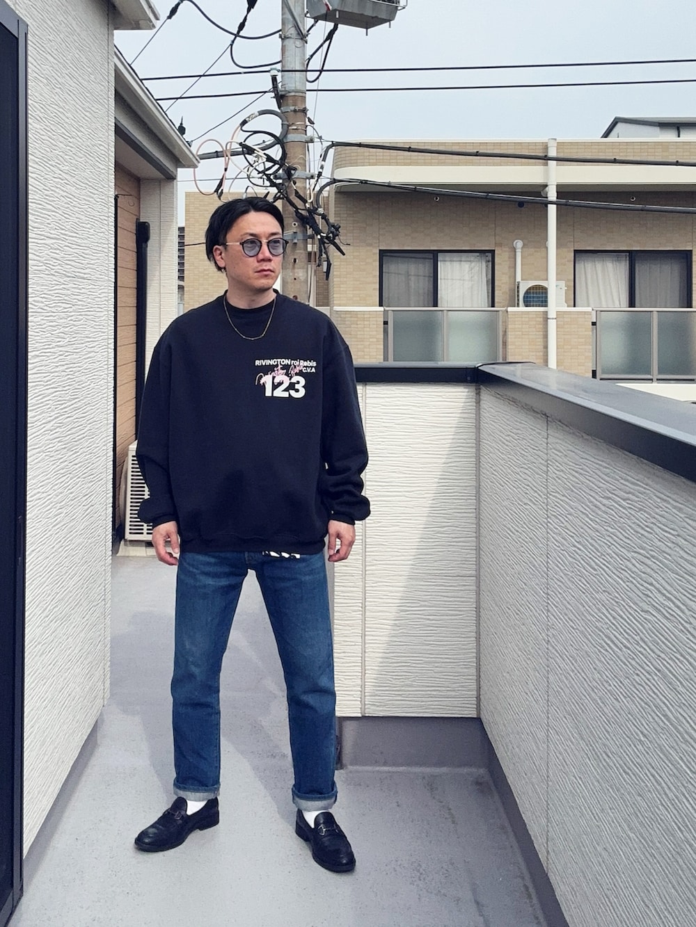 ブルー系のデニムパンツ、ブラック系のスウェット、ブラウン系のローファーを着用したメンズの春コーディネートの3枚目の写真