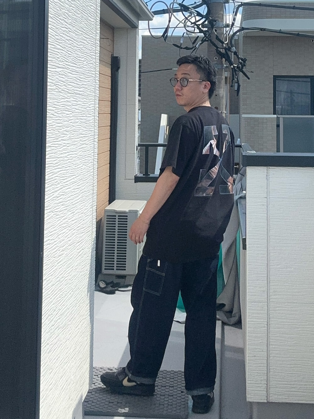 ブルー系のデニムパンツ、ブラック系のTシャツ/カットソー、ブラック系のスニーカーを着用したメンズの秋コーディネートの2枚目の写真