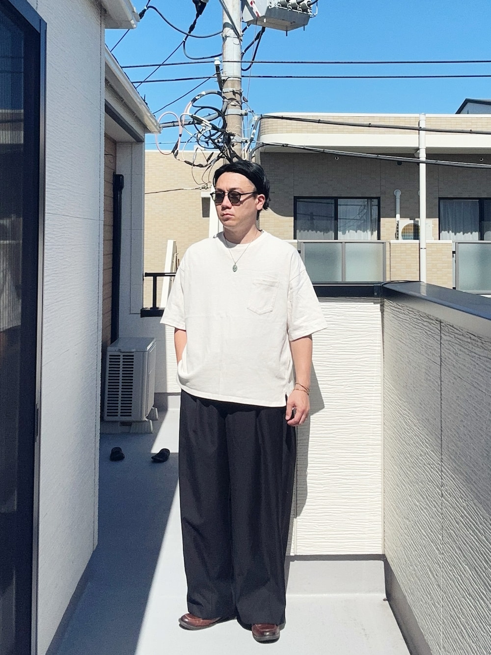ブラック系のスラックス、ホワイト系のTシャツ/カットソー、ブラウン系のローファーを着用したメンズの夏コーディネートの2枚目の写真