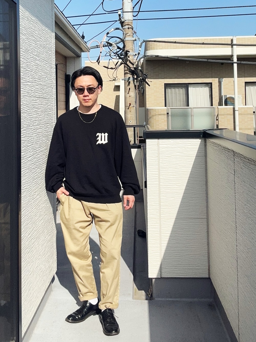 グリーン系のチノパンツ、ブラック系のスウェット、ブラック系のドレスシューズを着用したメンズの春コーディネートの2枚目の写真