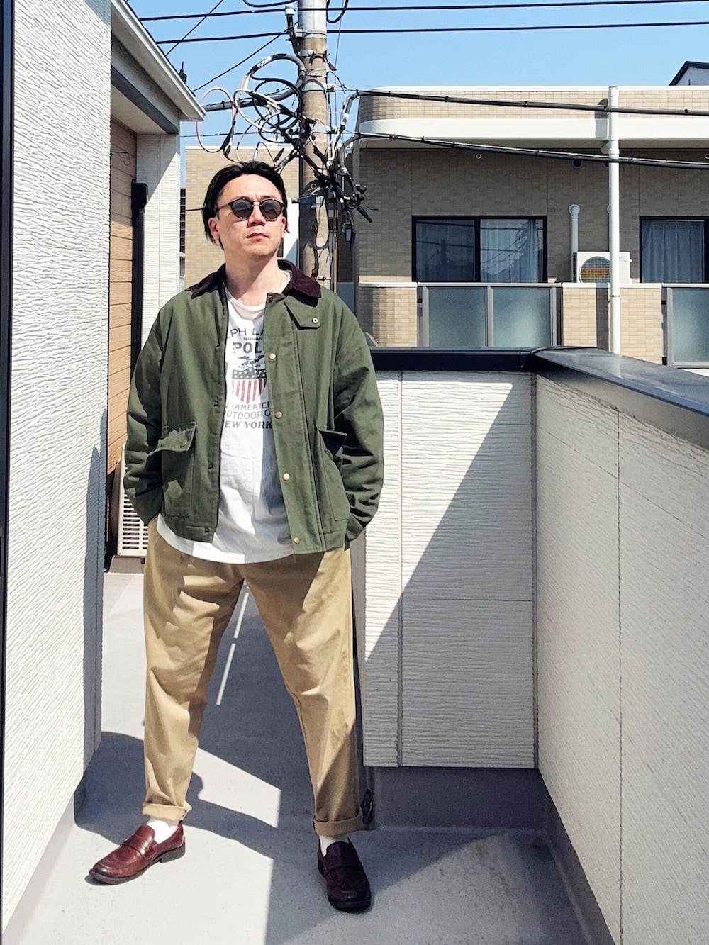 グリーン系のチノパンツ、ホワイト系のTシャツ/カットソー、グリーン系のミリタリージャケットを着用したメンズの春コーディネートの2枚目の写真